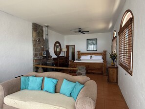A bedroom with a bed, a wooden dresser, a stone wall, a mirror, and a ceiling fan.