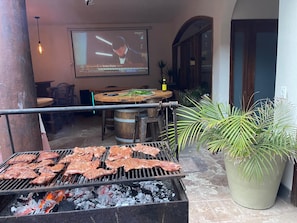 A grill with meat, a wooden table, chairs, and a potted plant. - Jacuzzi, Oceanfront Community Huge Ocean view 5 bedroom home gated 24/7 Security (Playas de Rosarito)