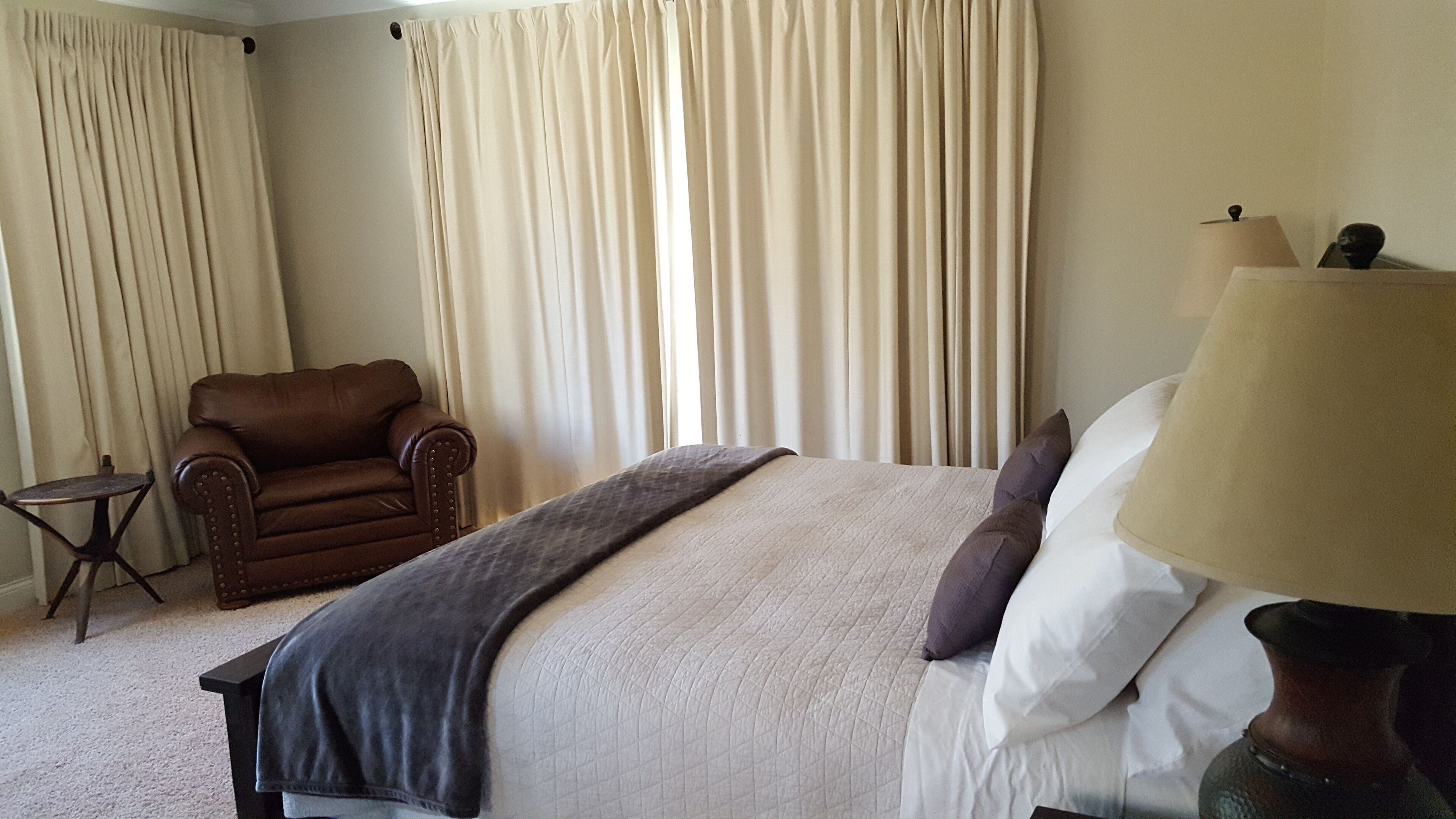 A hotel room with a bed, a chair, a lamp, and curtains.