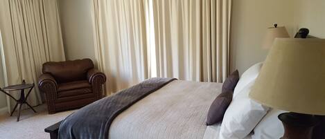 A hotel room with a bed, a chair, a lamp, and curtains.