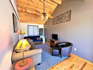 A cozy living room with a wooden ceiling, a sofa, a chair, a TV, and a fireplace. - #5 Buffalo Cabin at Ponderosa Place (Custer)