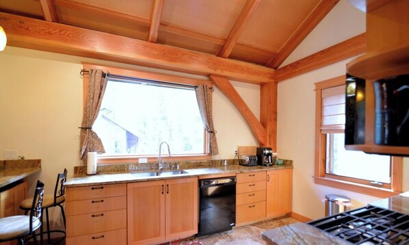 Une cuisine avec des meubles en bois, un lave-vaisselle, une cuisinière et une fenêtre avec des rideaux.