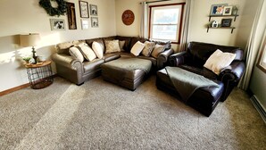 A living room with a sectional sofa, a coffee table, a lamp, a wall clock, a window with curtains, and a shelf with decorative items. - Great for EAA rental!
Less than 2.5 miles from EAA grounds! (Oshkosh)
