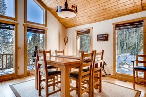 A wooden dining room with a large table and chairs, large windows with snowy views, and a 'Friends Always Welcome' sign.
