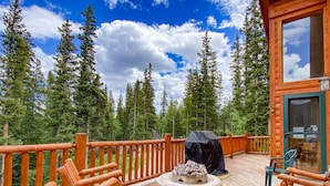 A wooden deck with a fire pit, outdoor seating, and a view of a forested area.
