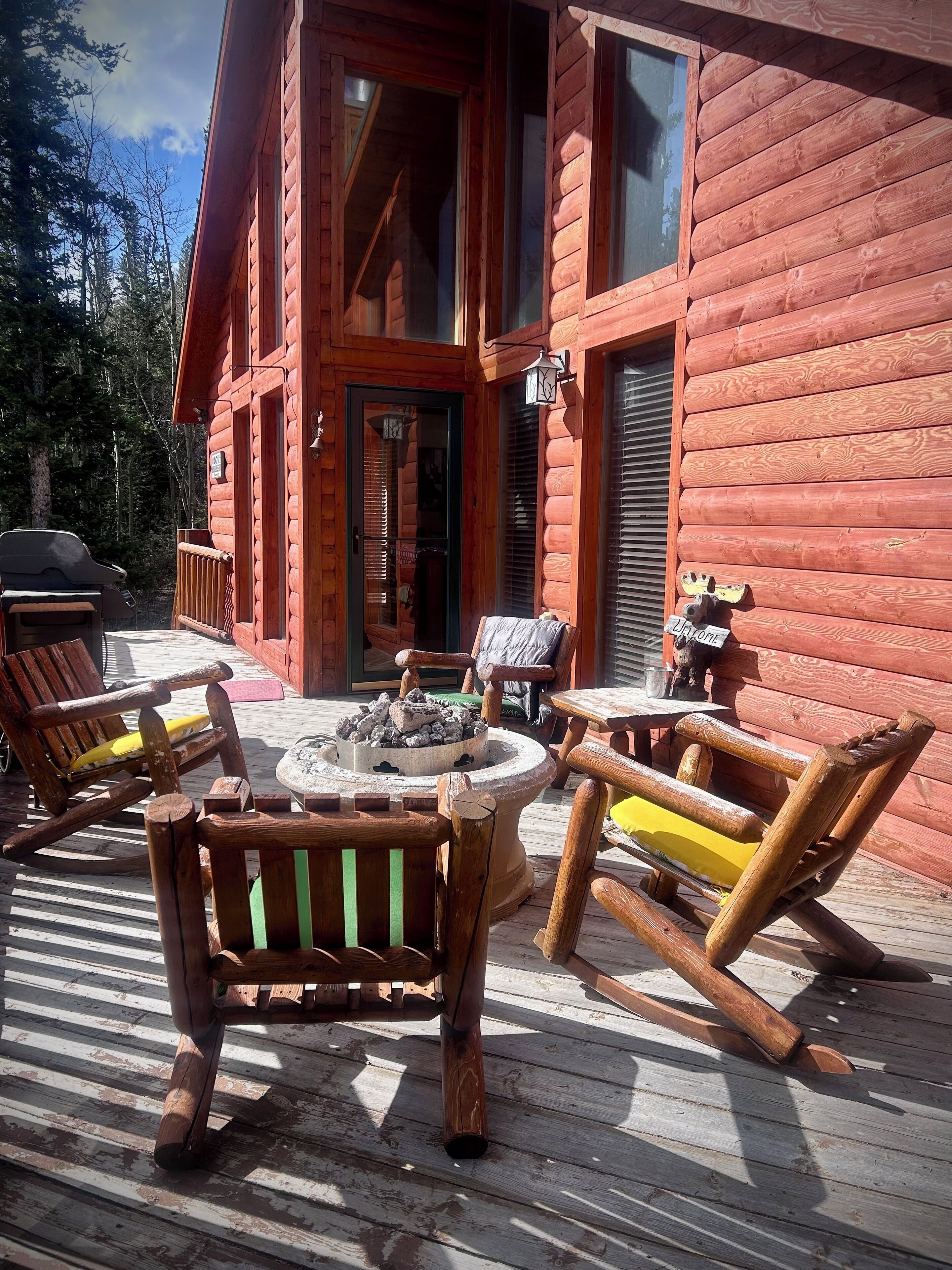 Une cabane en rondins dotée d’une terrasse aménagée avec du mobilier d’extérieur et un foyer.