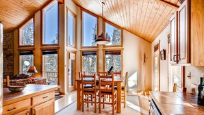A spacious kitchen with wooden cabinets, a dining table, and large windows offering views of the outdoors.