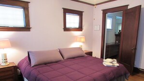A bedroom with a bed, two bedside lamps, a wooden nightstand, a door, and a window.