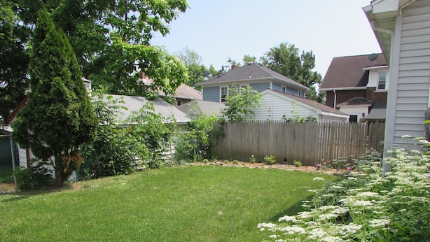 A well-maintained backyard with a grassy lawn, flowering plants, and a wooden fence.