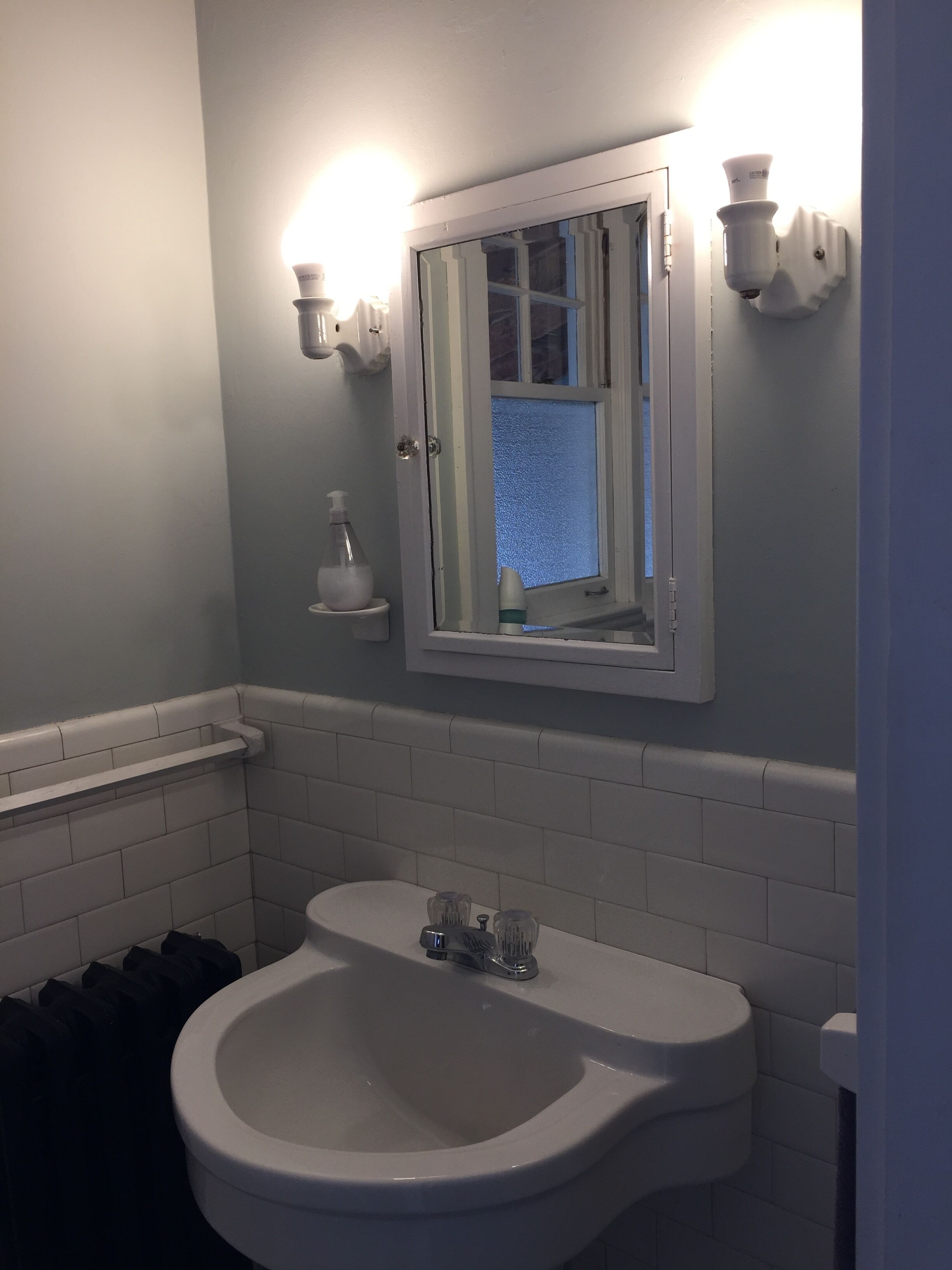 Een badkamer met een wit wastafelmeubel, een spiegel en twee wandlampen.