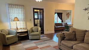 A living room with a sofa, two armchairs, a coffee table, a patterned rug, and a door leading to another room.