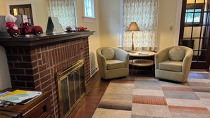 A cozy living room with a brick fireplace, two armchairs, a small table, and a lamp.