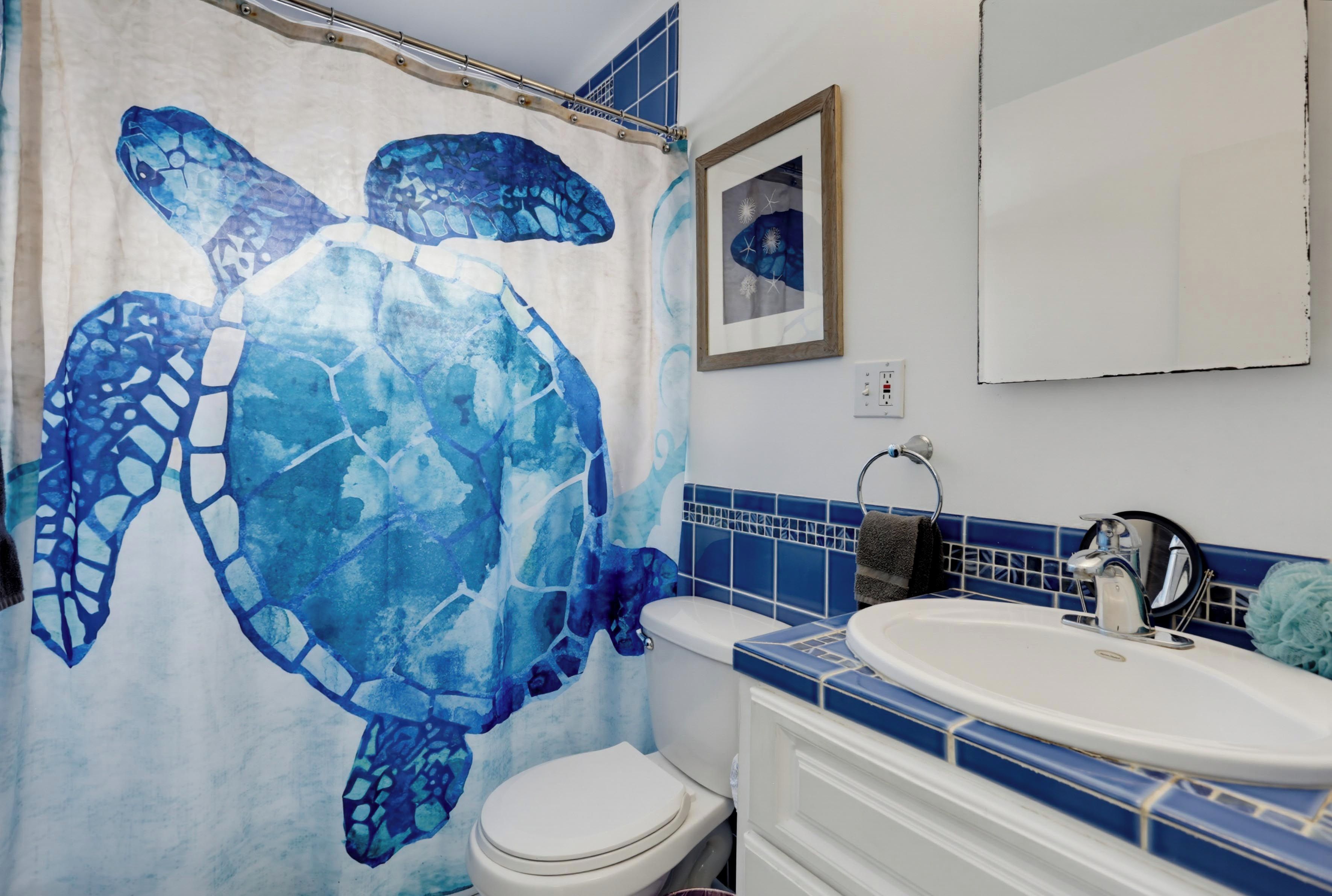Un baño con una decoración azul y blanca, un inodoro blanco, un lavabo con espejo y un cuadro en la pared.