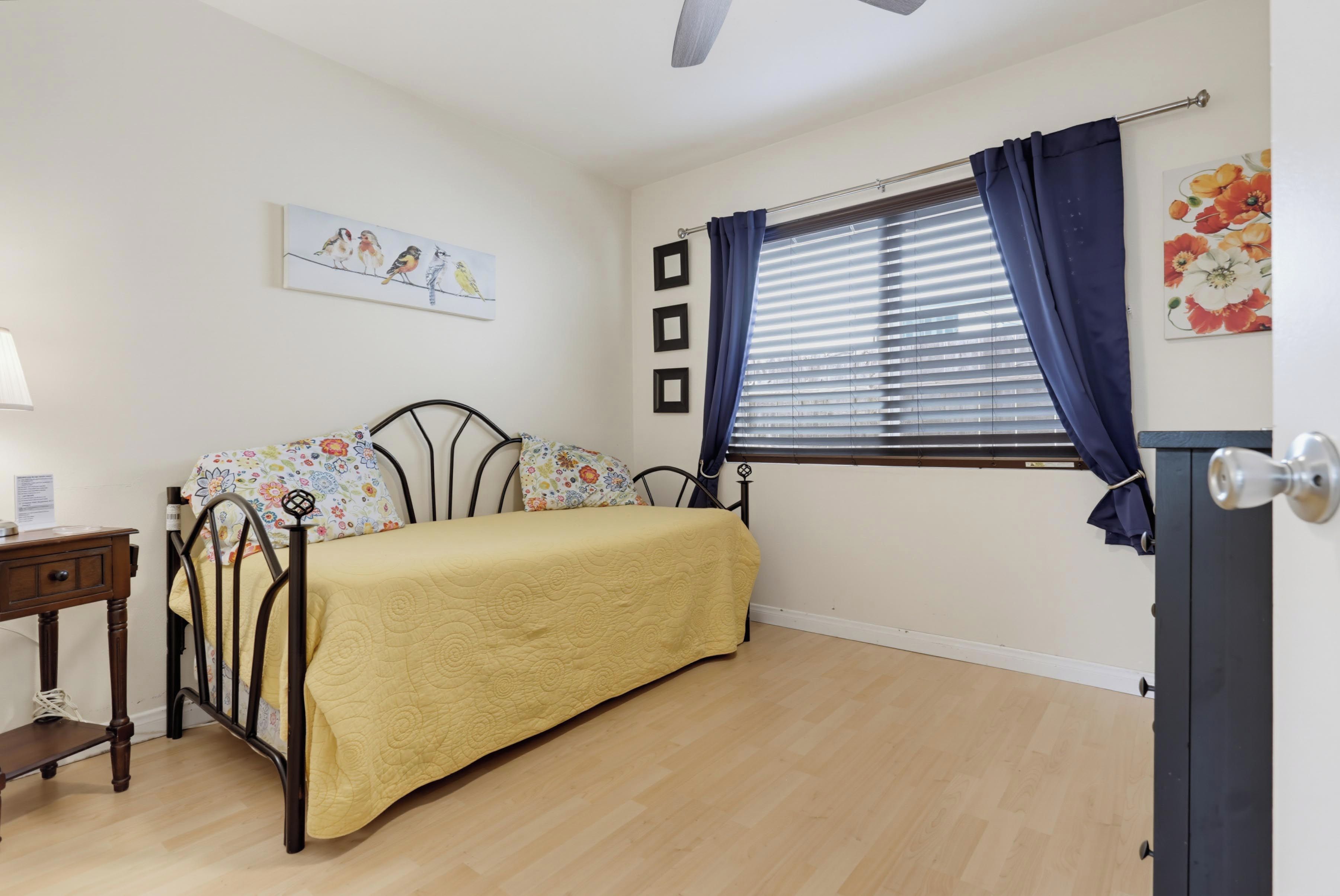 A bedroom with a bed, a nightstand, a window with curtains, a wall-mounted picture, and a door.