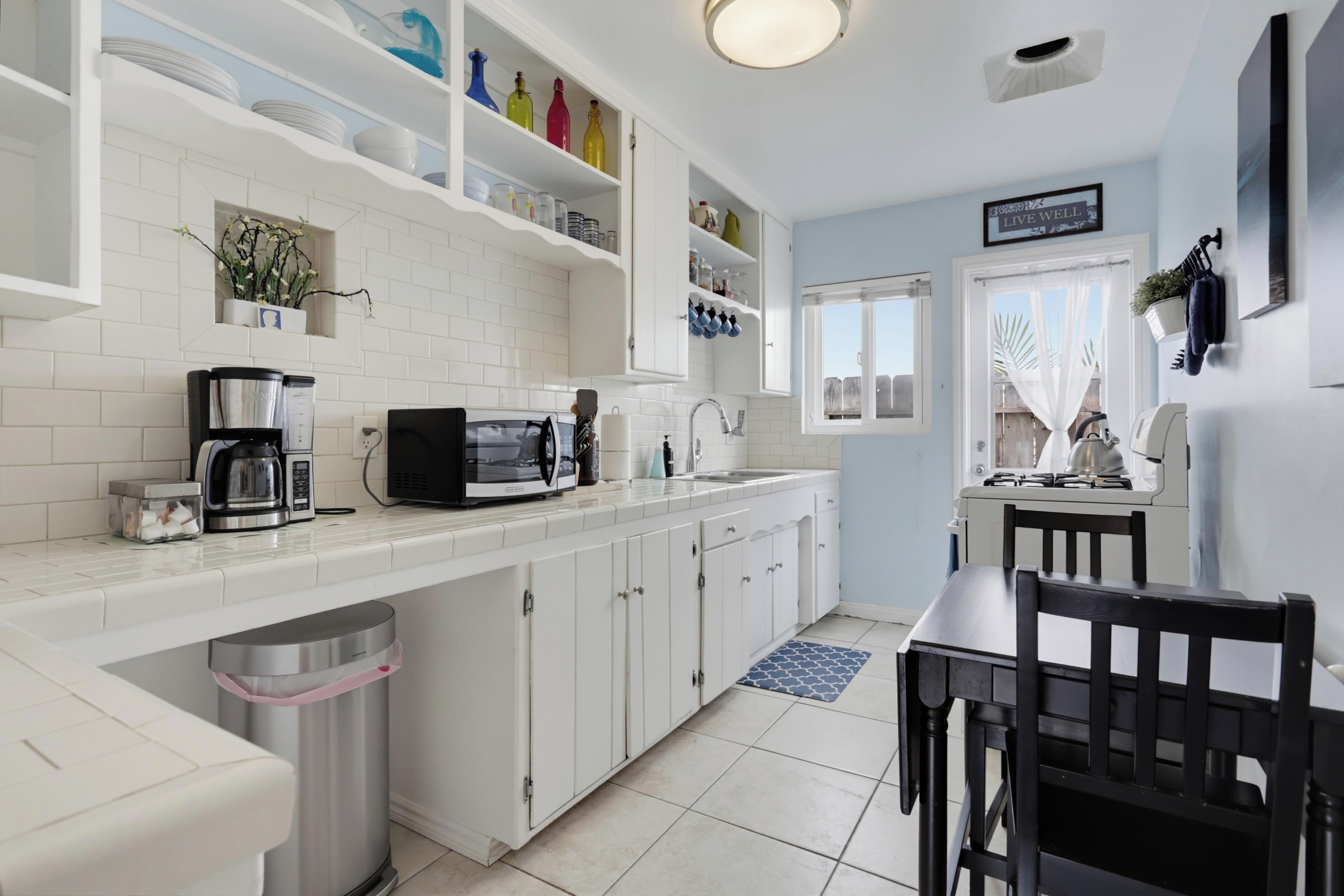 Una cocina moderna con armarios blancos, microondas integrado y cafetera.