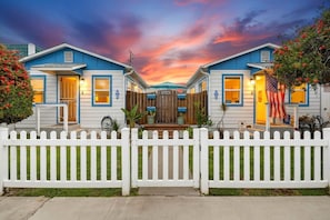 A row of two-story houses with a white picket fence, a wooden gate, and an American flag. - Charming Vacation Flat: 5-minute walk to beach! (San Diego)