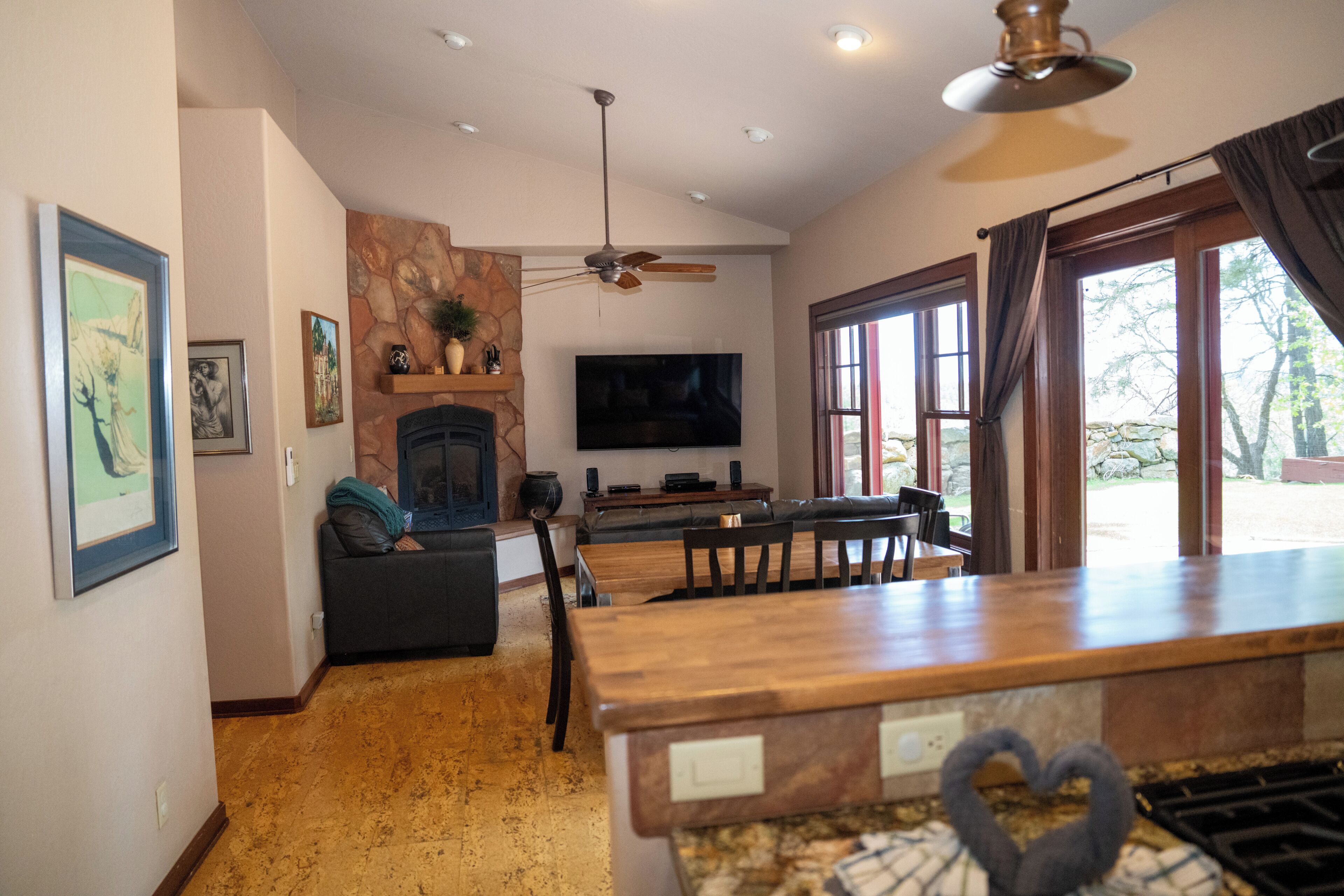 A living room with a fireplace, a television, a ceiling fan, and a dining area with a wooden table and chairs.
