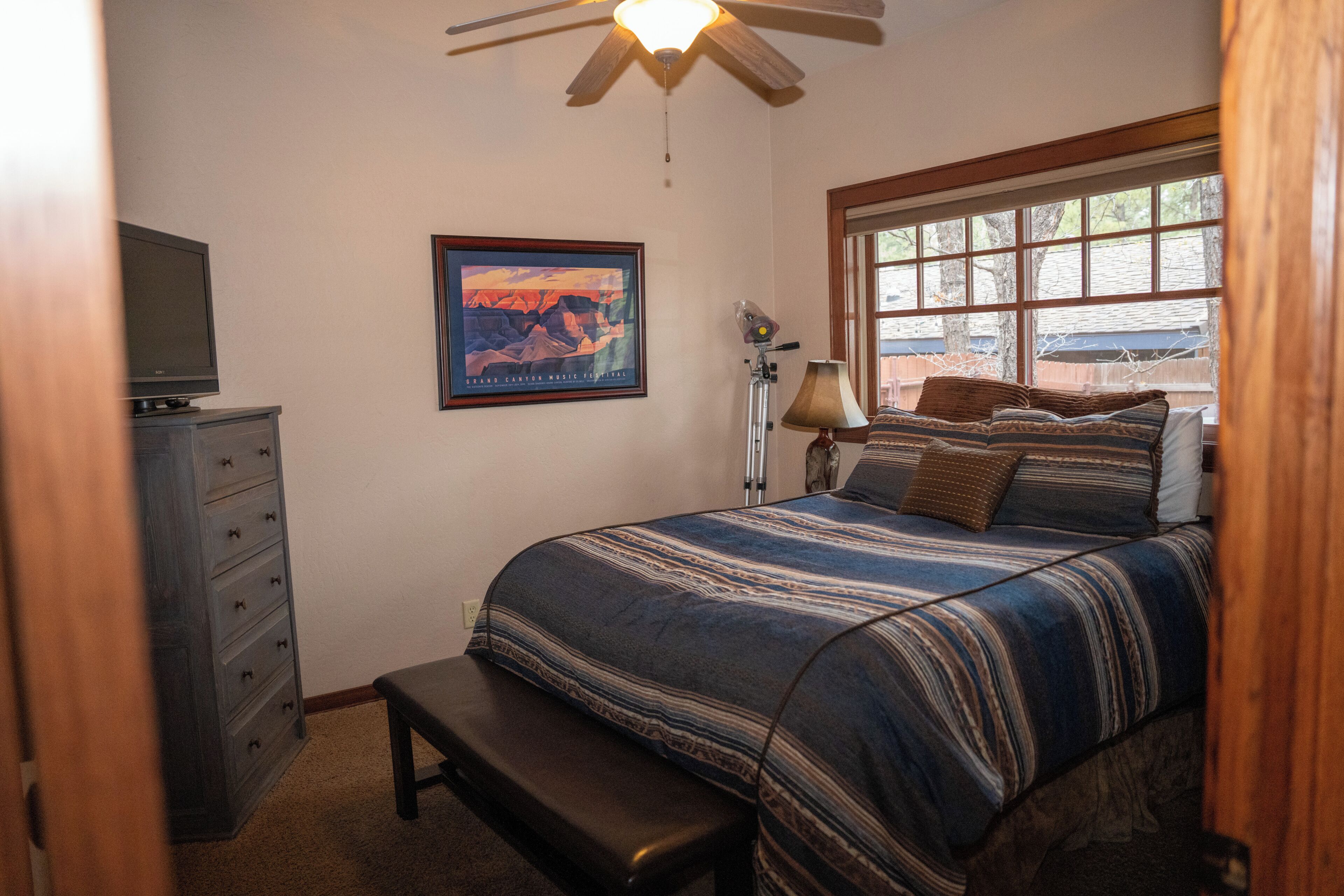 A bedroom with a bed, a desk, a chair, a television, a lamp, and a window.