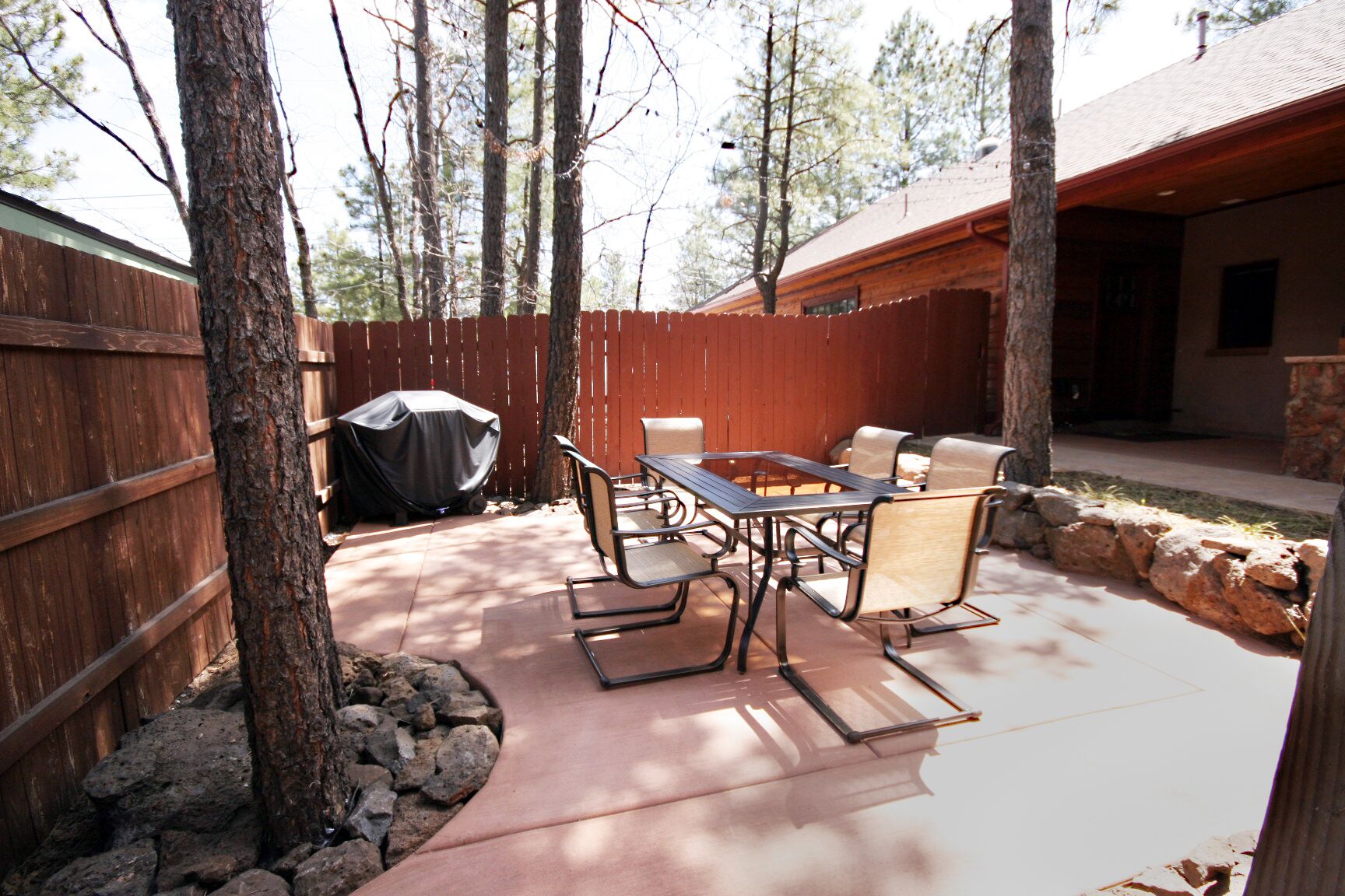 Un patio exterior con mesa y sillas, una parrilla cubierta y una valla de madera.