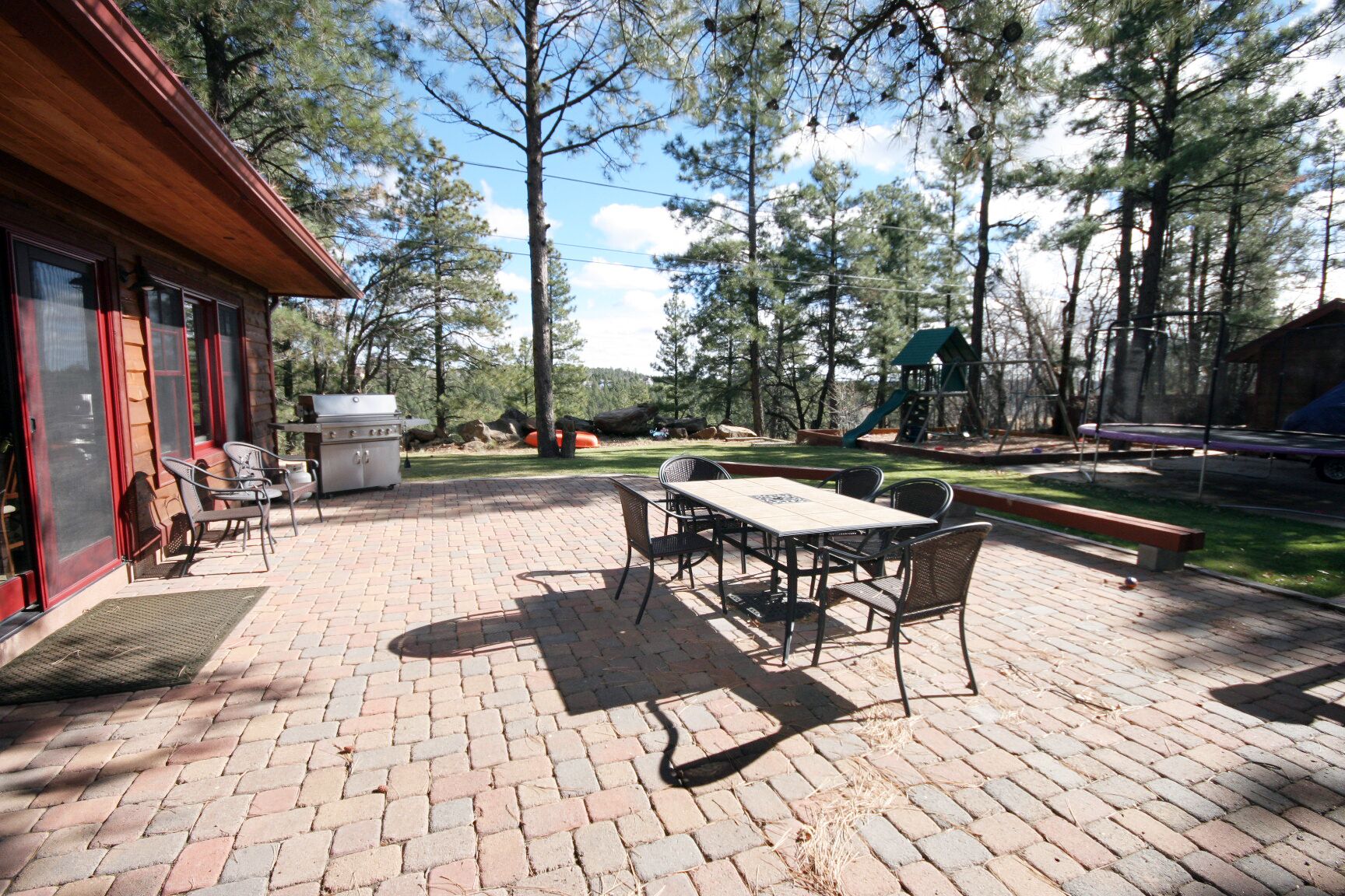 A patio area with a brick floor, outdoor seating, a grill, and a playground in the background.