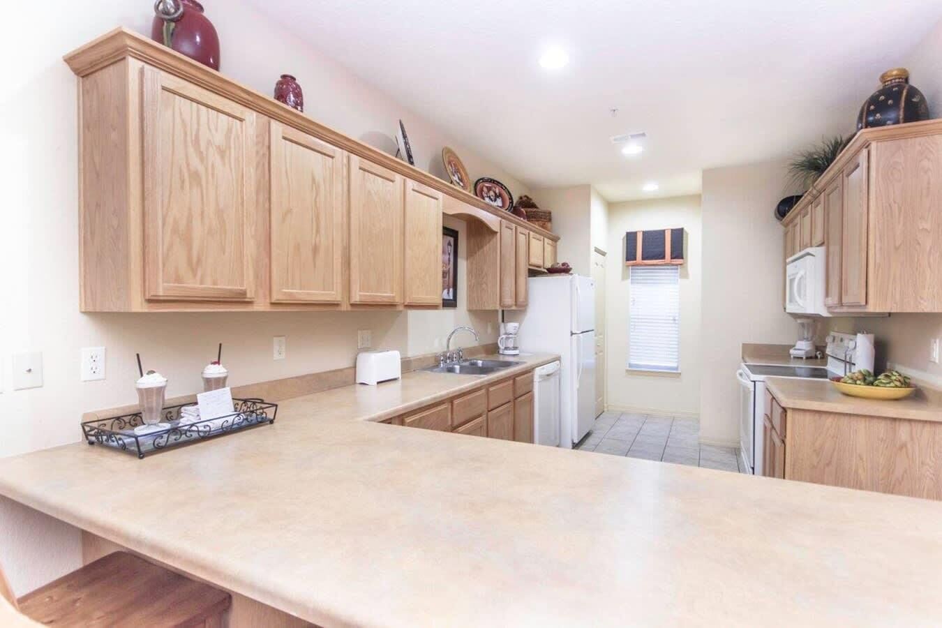 A kitchen with wooden cabinets, a countertop, a refrigerator, and a window with blinds.