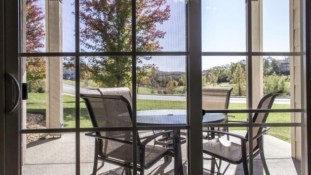 Eine Terrasse mit Tisch und Stühlen, Blick auf einen Golfplatz und ein Baum mit Herbstlaub.