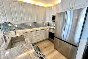 A modern kitchen with white cabinetry, a stainless steel refrigerator, and a patterned backsplash. - 3BR Beachfront Gem | Huge Balcony + Stunning Views | Nearly $100K Reno! (Orange Beach)