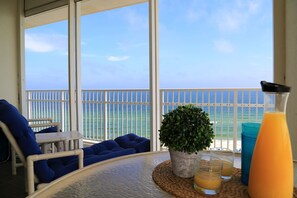 Un balcon avec vue sur l’océan, une table avec des boissons et des sièges bleus.