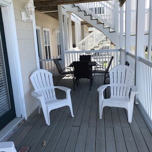 Un porche cubierto con sillas Adirondack blancas, una mesa y una escalera que conduce a un nivel superior.