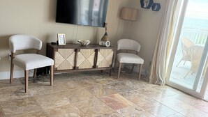 Una sala de estar con televisor de pantalla plana, dos sillones tapizados, un aparador tejido y vistas a través de un ventanal.