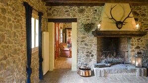 A stone-walled hallway with a fireplace, a deer head mounted above it, and a cozy seating area in the background.