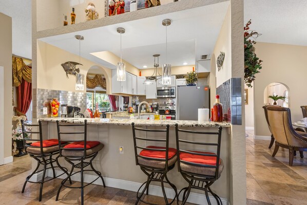 A modern kitchen with a central island, bar stools, and a dining area with a chandelier. - Luxurious Roman Style Pool Home in Brooksville Near Weeki Wachee and Beaches (Brooksville)