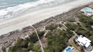 Vista aérea de una propiedad costera con playa, piscina y un camino que conduce a la playa.
