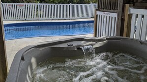Un jacuzzi con agua corriente, una piscina y una valla blanca con señales de advertencia.