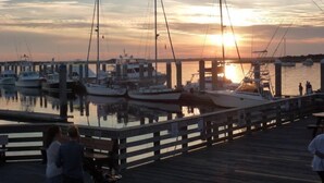 A marina at sunset with boats docked, a wooden pier, and a few people standing by.
