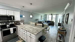 A modern kitchen with a marble countertop, stainless steel appliances, and a dining area with a white chair and table. - Ocean Village Vacation Rental, Golf view. Short walking distance to the beach.  (Hutchinson Island)