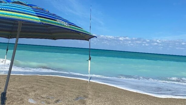 A beach with a colorful umbrella and a fishing rod. - Ocean Village Vacation Rental, Golf view. Short walking distance to the beach.  (Hutchinson Island)