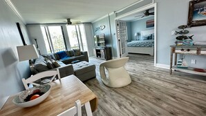 A modern living room with a wooden dining table, a sofa, and a chair. There is a TV and a cabinet in the background. - Ocean Village Vacation Rental, Golf view. Short walking distance to the beach.  (Hutchinson Island)