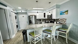 A modern kitchen with white cabinets, stainless steel appliances, and a marble island with bar stools. - Ocean Village Vacation Rental, Golf view. Short walking distance to the beach.  (Hutchinson Island)