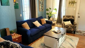 A living room with a blue sofa, a patterned armchair, a small table, and a radiator.