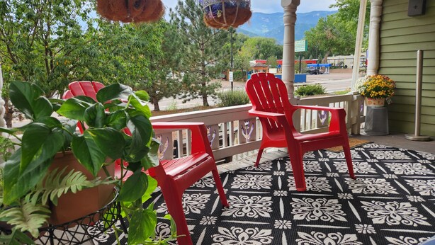 A porch with red chairs, hanging planters, and a view of a restaurant.