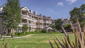 A multi-story hotel with balconies, a well-maintained lawn, and surrounding trees. - Sip, Taste, Hot Tub, Repeat - Full Resort Access - Sleeps 6 (Windsor)
