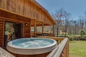Uma cabana de madeira com hidromassagem em um deck, com vista para uma área arborizada.