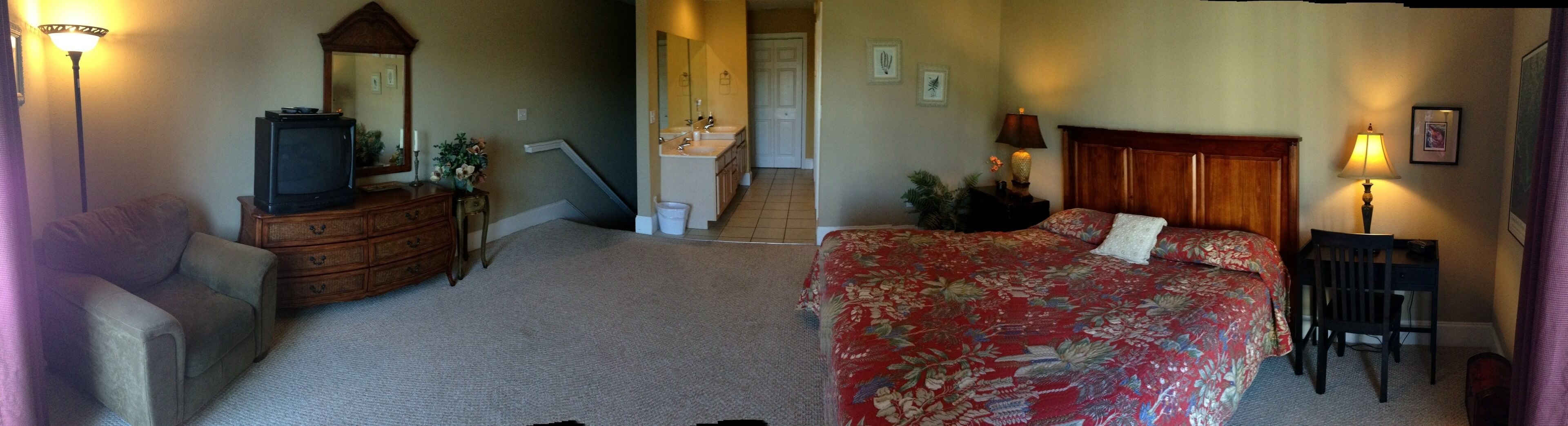 A bedroom with a bed, a dresser, a television, a mirror, and a staircase leading to a bathroom.