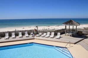 A pool area with lounge chairs and a gazebo overlooking a beach.