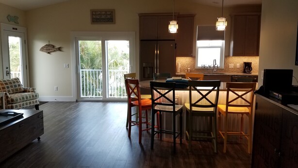A spacious living area with a dining table and chairs, a kitchen with a large island, and a sliding glass door leading to a balcony.