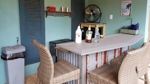 A bar area with wicker chairs, a bar counter, and bottles of alcohol.