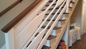 A staircase with wooden handrails and white steps, leading to a landing with a bed and storage boxes.
