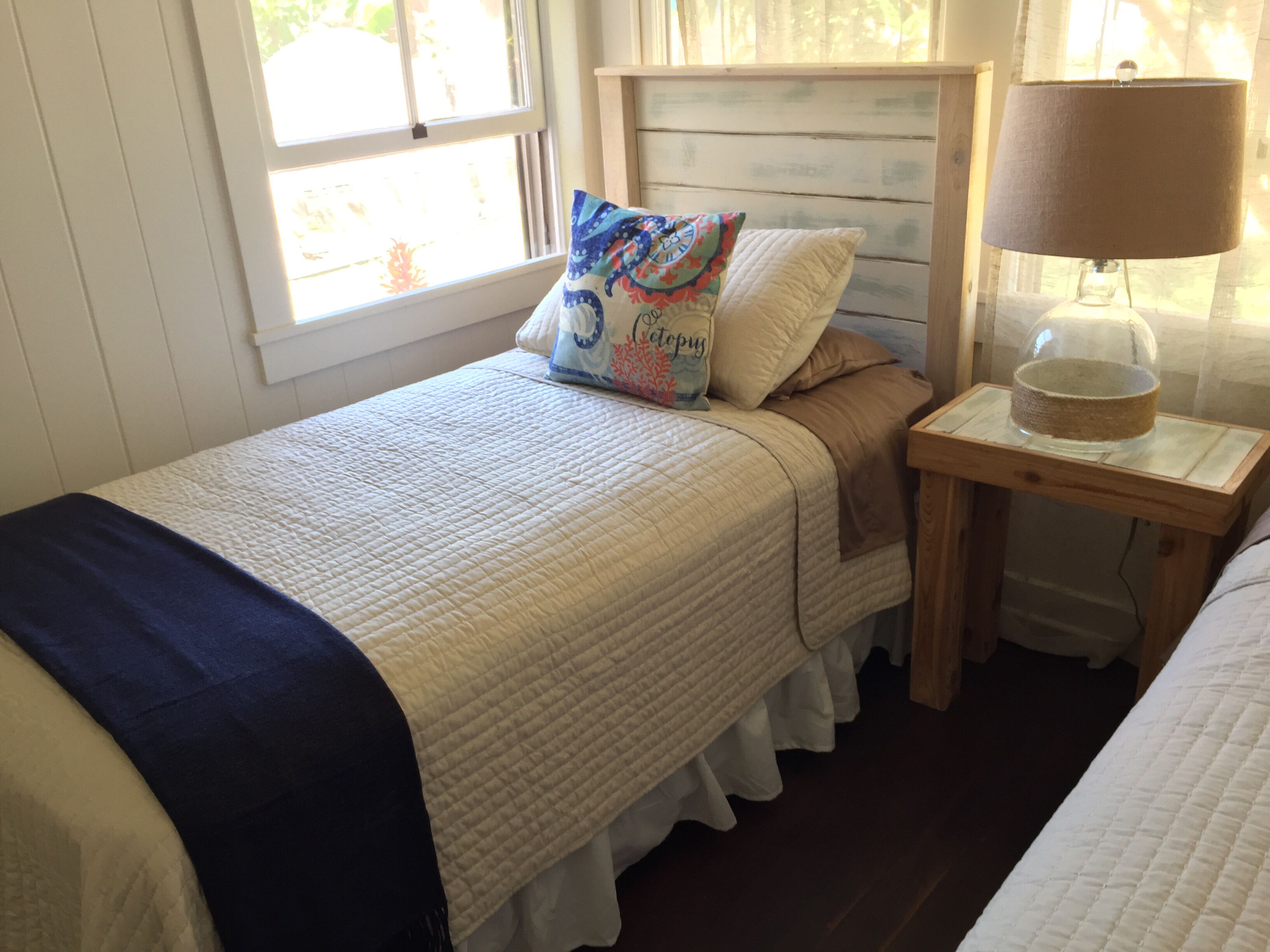 A bedroom with two beds, a nightstand with a lamp, and a window with curtains.