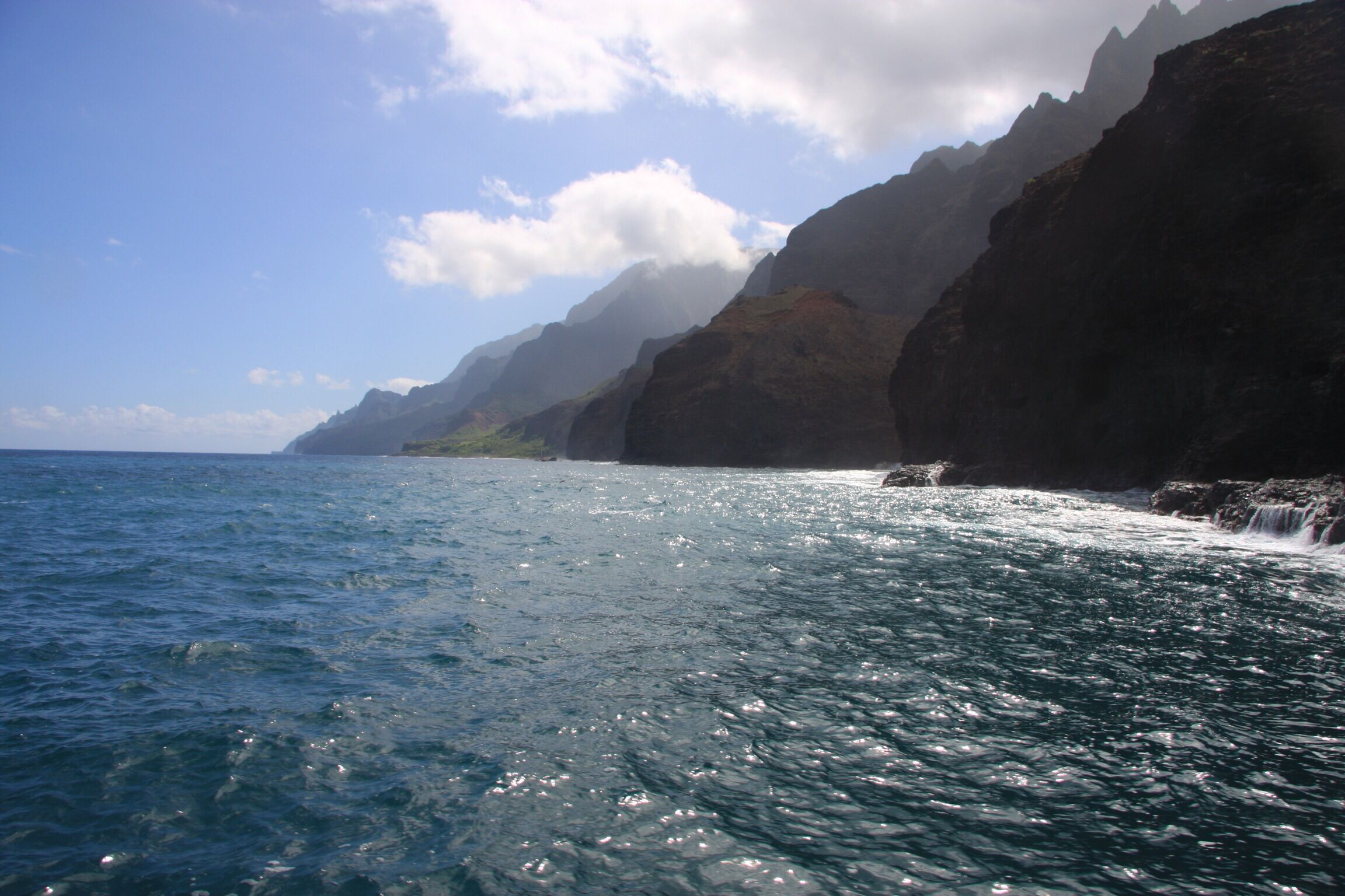 A coastal scene with clear blue water, rocky cliffs, and a distant shoreline.